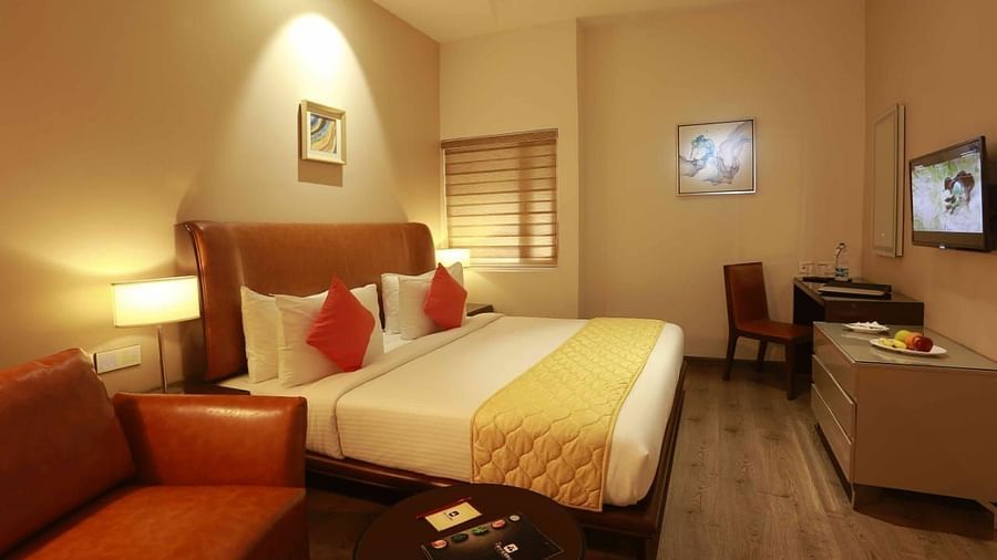 Executive Room at Mayberry Tiruppur with a bed, TV stand with a wall-mounted TV, a table with a chair, and a sofa